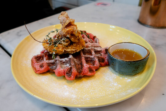 Pink waffle with deep-fried chicken and maple syrup