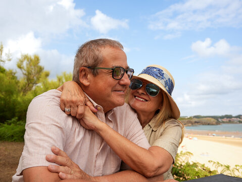Senior couple embrace on beach during sunny vacation