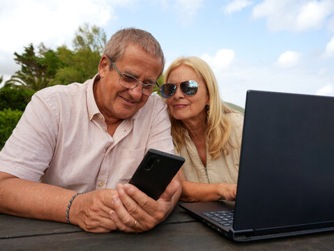 Senior couple use smartphone and laptop at beach resort