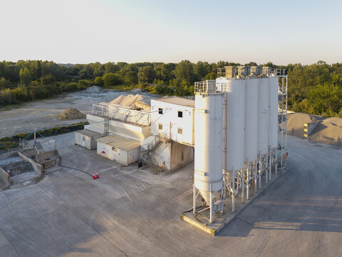 Aerial view of a concrete batching plant with white silos and industrial facilities surrounded by piles of gravel and trees in Krakow, Lesser Poland Voivode, Poland.
