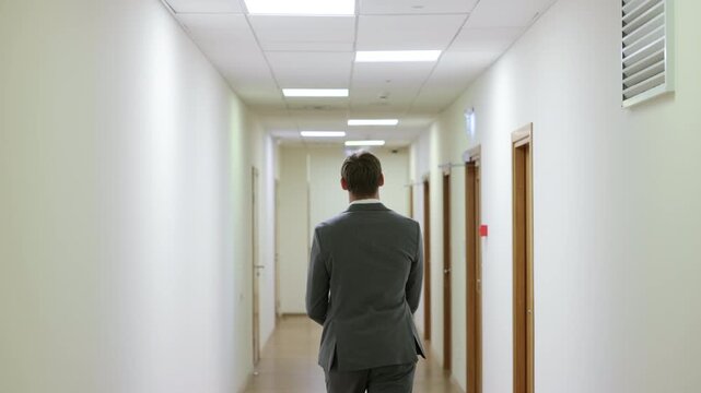Successful male executive in a formal suit walking through a bright corporate hallway directly towards the camera.Split screen or sequence of a professional businessman walking back and forth in a con
