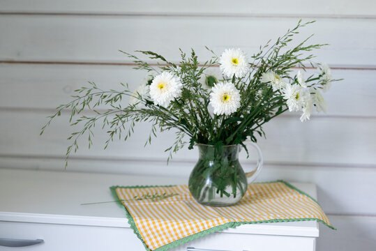 White flower bouquet in glass pitcher on wooden table