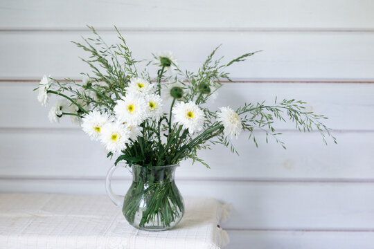 White flower bouquet in glass pitcher on rustic table