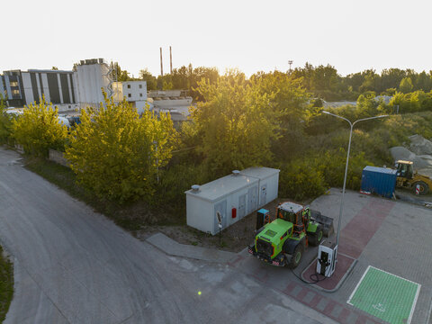 Aerial view of an electric construction loader charging at a station in an industrial area with trees and buildings in the background in Krakow, Lesser Poland Voivodeship, Poland.