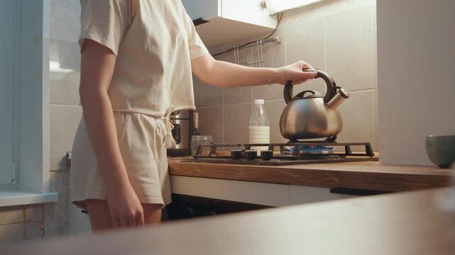 Kitchen closeup lifting kettle over flame focused home cook lifts metal kettle, steam and scent build, whistling moment at tiled backsplash with utensils and quiet brewing ritual.