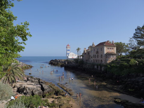 View of the Santa Marta Lighthouse and the rocky cove with people swimming in the clear water in Cascais, Lisbon, Portugal.