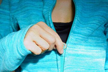 Woman's hand pulling zipper of teal fleece jacket closed at chest level while getting ready to leave home for hiking trip. Conveys cool-weather dressing and practical layering for active recreation. © tanyatorgonskaya