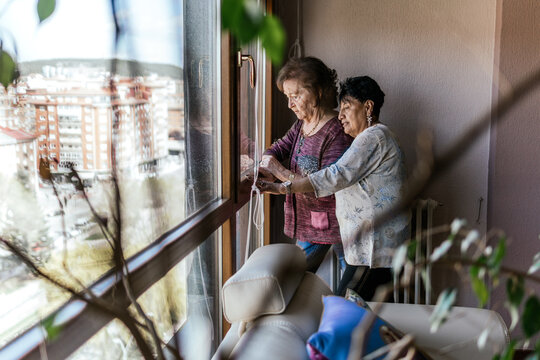 Elderly women look through window together at home