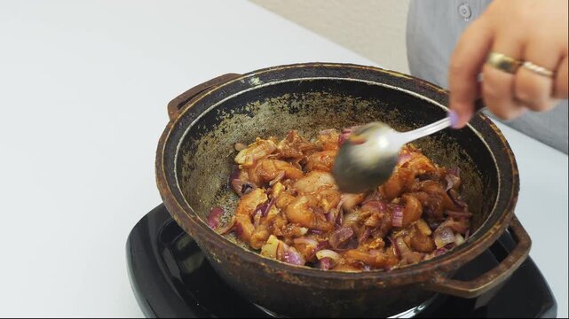 Pieces of chicken fillet with onion marinated in soy sauce and spices are fried in a frying pan. Medium shot.