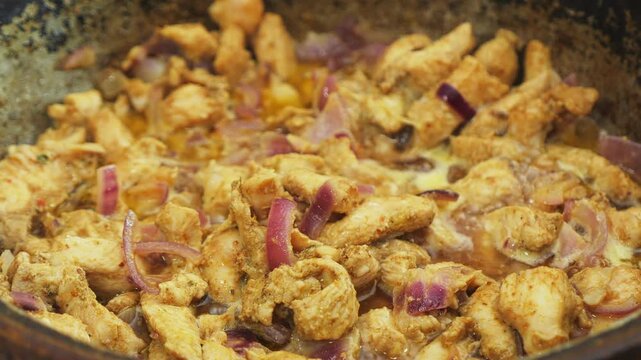 In a deep cast-iron skillet, onions simmer with chicken in sauce and spices. Medium shot.