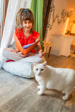 Woman with dreadlocks read beside white cat at home