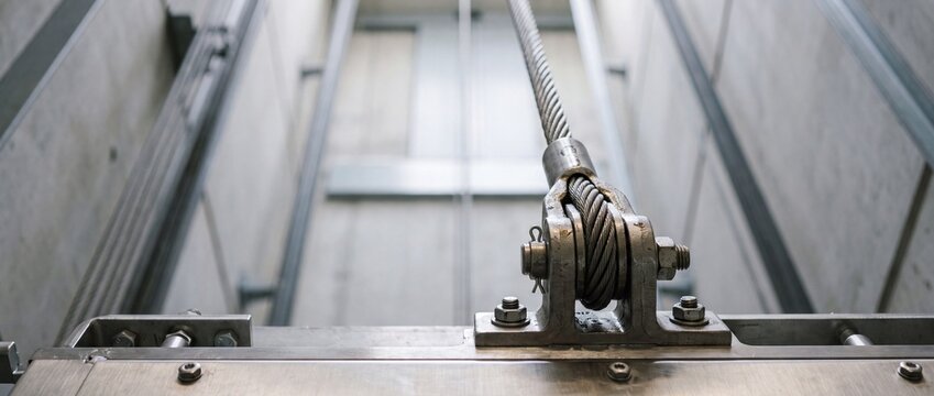 Closeup of elevator cable and pulley mechanism in industrial lift shaft with steel hardware