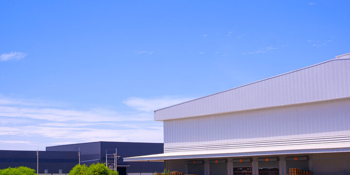 Modern warehouse with multiple loading bay shutter doors with industrial building under blue sky. Logistics, distribution, and supply chain facility structure for shipping
