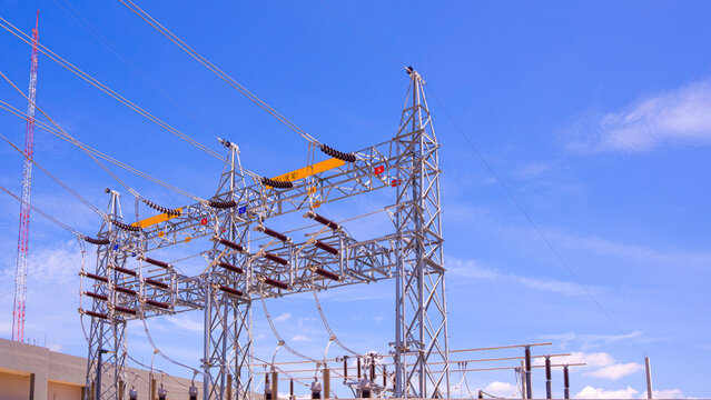 High voltage electrical substation power lines on steel gantry structure against blue sky. Energy distribution background.