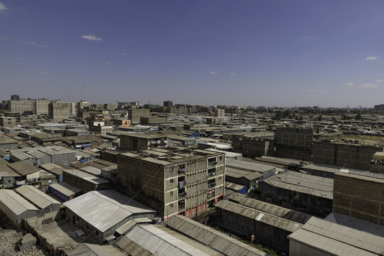 View of the dense urban landscape of Nairobi featuring rows of corrugated metal roofs, multi-story concrete residential buildings, and clear blue sky in Nairobi, Nairobi County, Kenya.