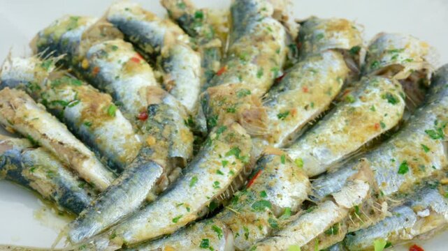 Sardines marinating in olive oil and fresh chopped herbs, presented as a healthy appetizer or main course close-up