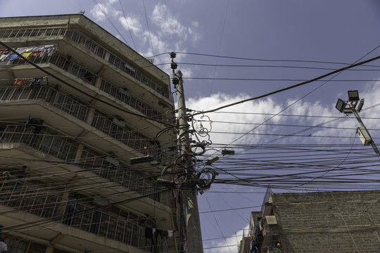 View of a utility pole densely packed with tangled electrical wires and cables in an urban setting, with a residential building in Nairobi, Nairobi County, Kenya.