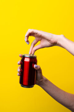 Female hand open red beverage can on yellow background