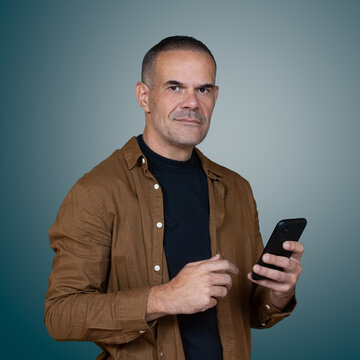 Middle aged man holding smartphone and looking at camera in studio portrait with copy space, representing mobile technology and digital communication.
