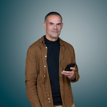 Middle aged man holding smartphone and looking at camera in studio portrait with copy space, representing mobile technology and digital communication.