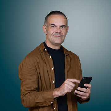 Confident middle aged man using smartphone, looking at camera in studio portrait with copy space, modern technology and digital communication concept.