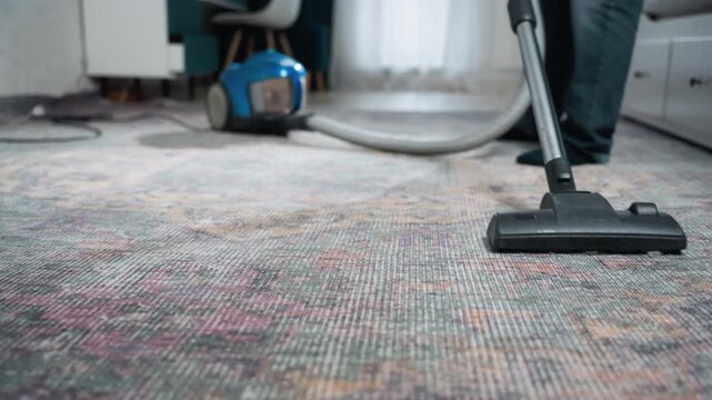 Professional house vacuum deep clean action, wide view focuses on powered canister unit and operator moving with efficient strokes, cord trailing across patterned floor, rapid suction removes stains,