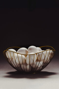White egg collection in gold wire basket on dark background