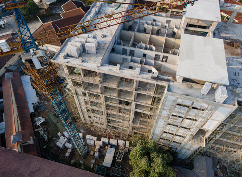 Aerial view of a multi-story building under construction with a large yellow tower crane, scaffolding, and stacks of building materials in Banyumas Regency, Central Java, Indonesia.