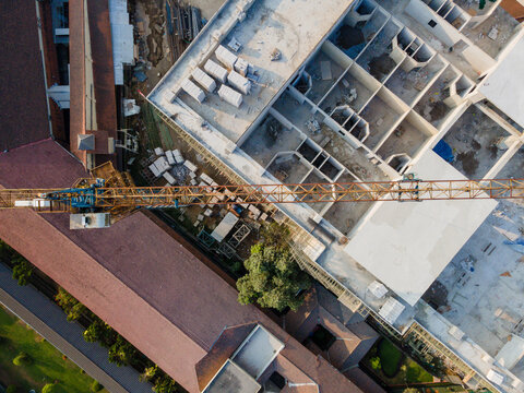 Aerial view of a construction site with a large crane hovering over a building structure, surrounded by rooftops and greenery in Banyumas Regency, Central Java, Indonesia.