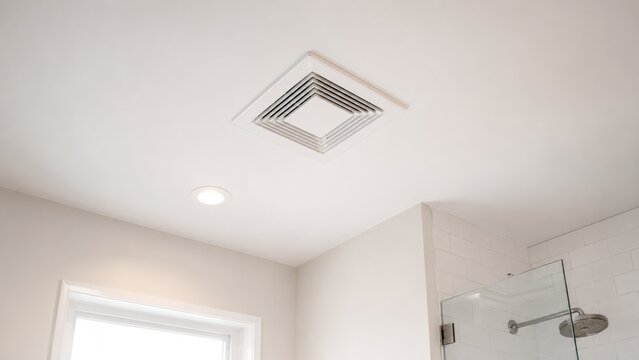 Bright modern bathroom ceiling with a square ventilation grille, recessed light, window light, and part of a glass shower and tiled wall