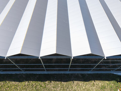 Aerial view of a greenhouse structure under construction with metal framing and white roof panels over a grassy field in Poland.