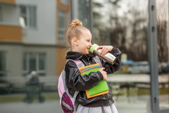 Elementary school student drinking from reusable water bottle with backpack and books