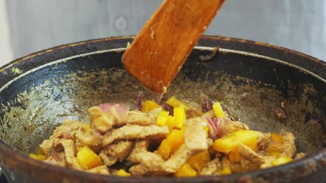 In a deep cast-iron skillet, onions and chicken simmer in a sauce with spices and pepper. Medium shot.