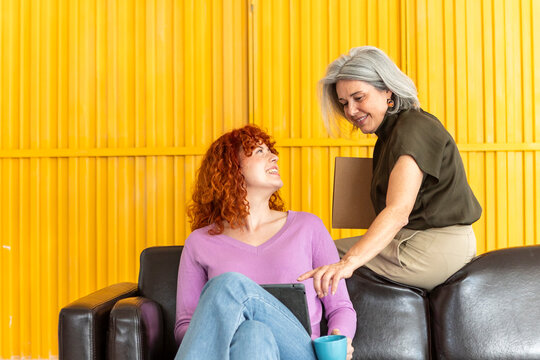 Mature businesswoman helping colleague with tablet on sofa