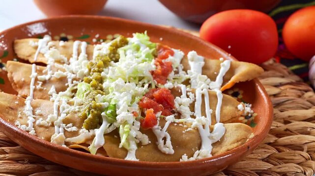 Close-up of traditional Mexican golden fried chicken molotes or flautas on a rustic clay plate with red and green salsa, lettuce, cream and fresco cheese