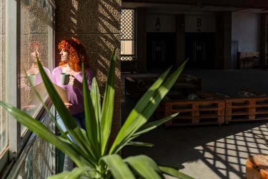 Young businesswoman with coffee and folder by sunlit window
