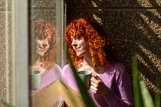 Red-haired businesswoman enjoying coffee by window reflection