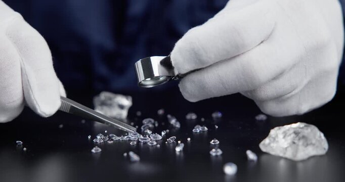 Gloved jeweler hands inspecting loose diamonds on black tabletop in studio with loupe and tweezers.