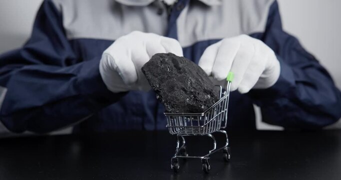 Slow motion worker presenting miniature shopping cart with lump of coal on table while changing thumb gesture.