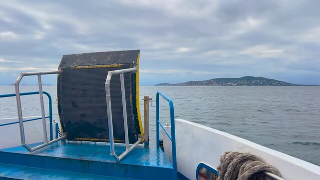 View from the bow of a passenger ferry approaching Buyukada in Istanbul under dramatic overcast sky, Marmara Sea waves and historic island architecture ahead and maritime transport
