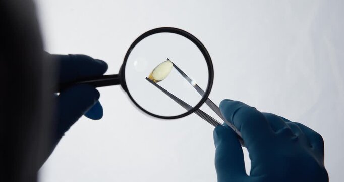 Gloved hands inspecting small lens with magnifier in studio setting.