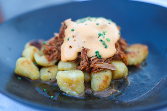 Golden gnocchi topped with tender braised beef and creamy sauce sits on a dark plate, capturing rich texture, savory flavor, and refined Mediterranean comfort cuisine.