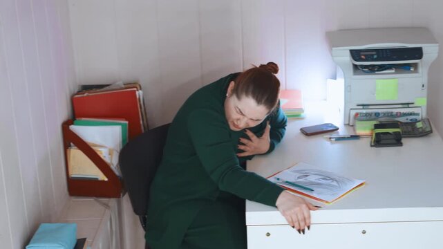 White woman clutching chest and reaching across desk, sudden gasp and visible distress in small home office, attempts to call for help with papers and phone nearby, urgent mood and raw emotional
