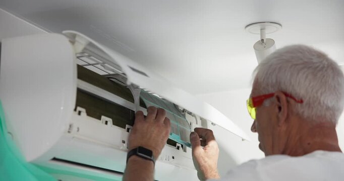 Slow motion man inspecting and removing air conditioner filter in home living room near ceiling.