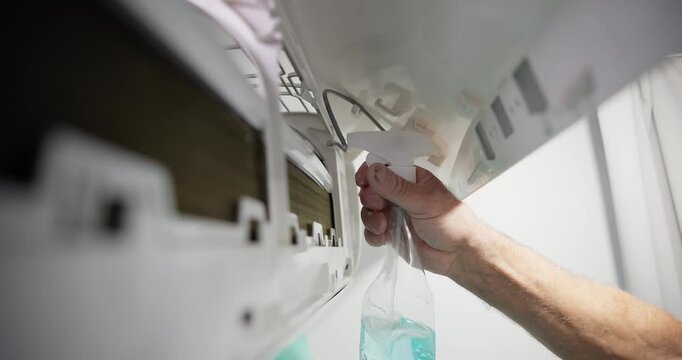 Worker Hand spraying cleaning solution into indoor wall mounted air conditioner unit during routine maintenance handheld pan tilt.