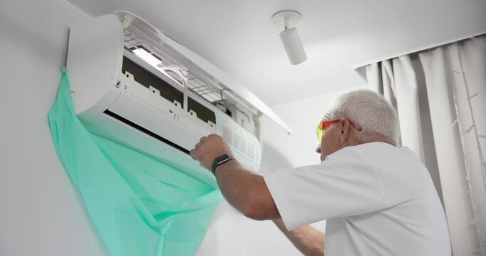 Slow motion technician inspecting and replacing filter in indoor split air conditioner unit in living room near window and curtain.