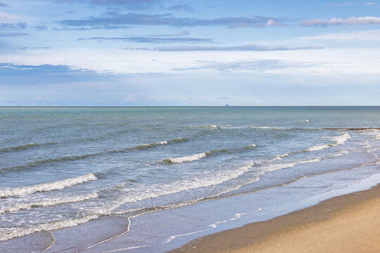 Panoramic view of tranquil sea waves gently breaking on a deserted sandy beach under a soft sky with delicate cloud formations. Ostend town in Belgium, Europe.