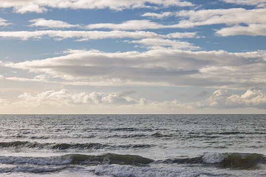 Expansive blue sea with gentle waves under a dynamic sky filled with white and gray clouds, evoking a sense of calm. Ostend town in Belgium, Europe.