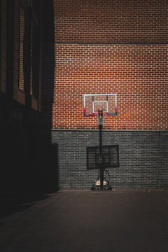 View of a basketball hoop mounted on a two-tone red and dark grey brick wall on an asphalt court in Philadelphia, Pennsylvania, United States.