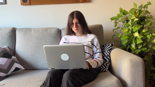 Stressed teenager experiencing fatigue and emotional burnout during a remote learning session or video call while sitting on a sofa with her laptop at home